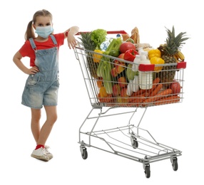 Little girl in medical mask with shopping cart full of groceries on white background