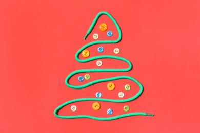 Photo of Christmas tree made of shoe lace and different buttons on red background, flat lay