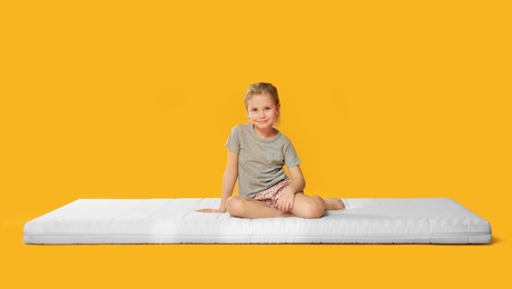 Photo of Little girl sitting on mattress against orange background