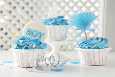 Photo of Delicious cupcakes with light blue cream and toppers for baby shower on white table