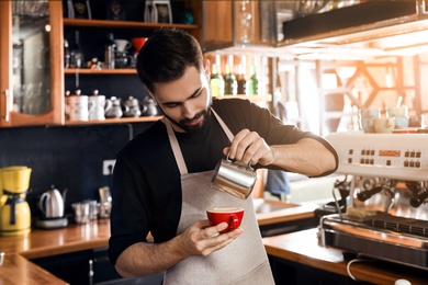 Barista pouring milk into cup of coffee in shop