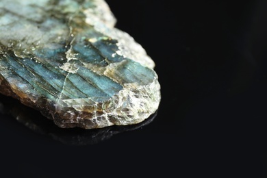Photo of Beautiful labradorite gemstone on black background, closeup. Space for text