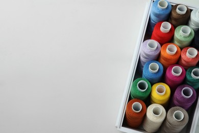 Photo of Box with colorful sewing threads on white marble table, top view. Space for text