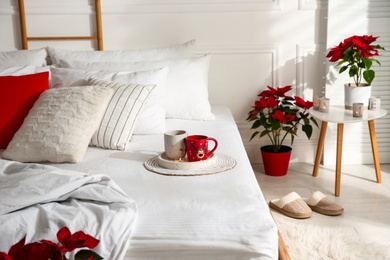 Poinsettias near bed in light cozy room. Christmas Interior design
