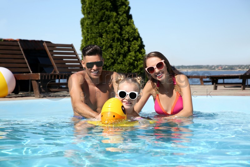 Happy family with inflatable ring in outdoor swimming pool on sunny summer day