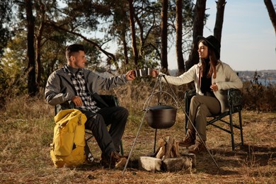 Photo of Couple resting in camping chairs and enjoying hot drink near bonfire outdoors