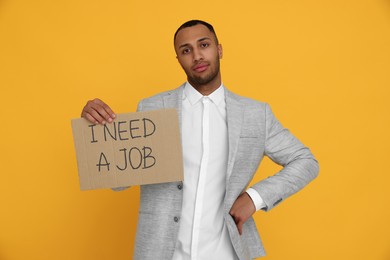 Photo of Young unemployed man holding sign with phrase I Need A job on yellow background