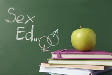 Books and apple near chalkboard with phrase "Sex ed"