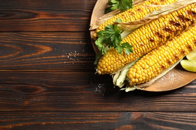 Delicious grilled corn cobs on wooden table, top view. Space for text