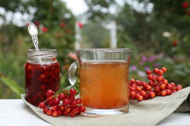 Photo of Cup of tea, jam and ripe viburnum berries on table outdoors