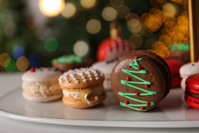 Beautifully decorated Christmas macarons on white table against blurred festive lights, closeup. Space for text