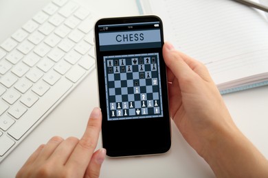 Woman playing online chess on smartphone at table, closeup