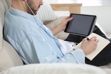 Photo of Young man with headphones using modern tablet for studying at home, closeup. Distance learning
