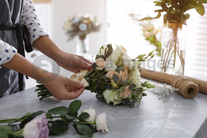 Florist tieing bow of beautiful wedding bouquet at light grey marble table, closeup