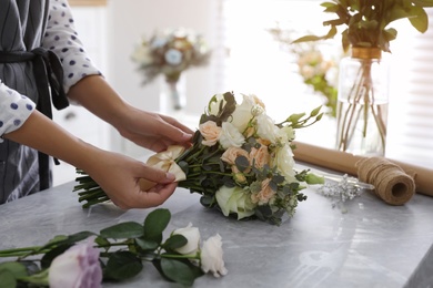 Florist tieing bow of beautiful wedding bouquet at light grey marble table, closeup