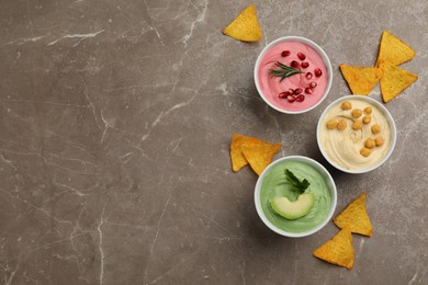 Different delicious hummuses with tortilla chips on brown marble table, flat lay. Space for text