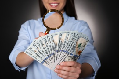 Photo of Expert authenticating 100 dollar banknotes with magnifying glass against dark background, closeup. Fake money concept