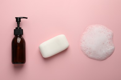 Dispenser and soap bar with fluffy foam on pink background, flat lay