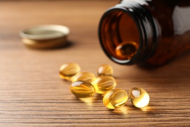 Photo of Overturned bottle with dietary supplement capsules on wooden table, closeup