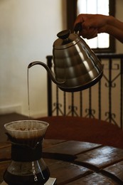 Photo of Barista pouring water from kettle into cup with coffee and wave dripper in cafe, closeup