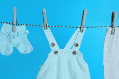 Different baby clothes drying on laundry line against light blue background, closeup