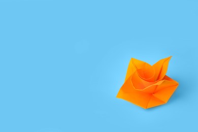 Photo of Origami art. Handmade orange paper flower on light blue background, space for text