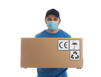 Courier in mask holding cardboard box with different packaging symbols on white background. Parcel delivery