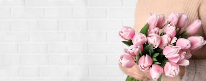 Woman with beautiful pink spring tulips near white brick wall, space for text. Horizontal banner design