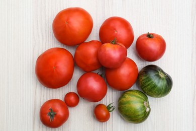 Many different ripe tomatoes on white wooden table, flat lay