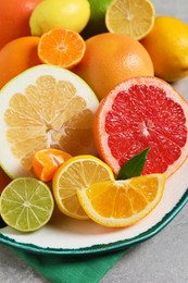 Photo of Plate with different citrus fruits and fresh leaves on light grey table, closeup