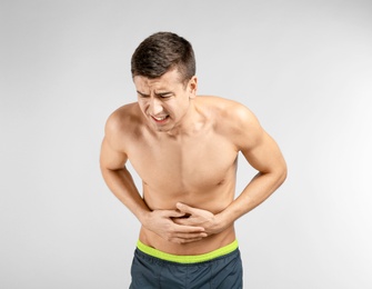 Young man suffering from abdominal pain on light background