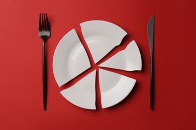Pieces of broken ceramic plate and cutlery on red background, flat lay
