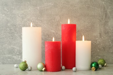 Burning candles with Christmas baubles on light grey table