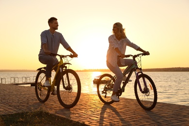 Lovely couple riding bicycles on embankment at sunset