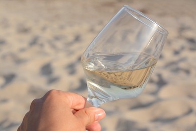Photo of Woman holding glass of tasty wine on sand, closeup