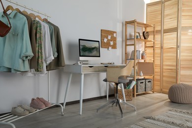 Stylish room interior with comfortable workplace and rack of clothes