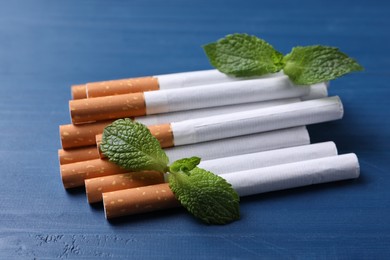 Menthol cigarettes and mint leaves on blue wooden table