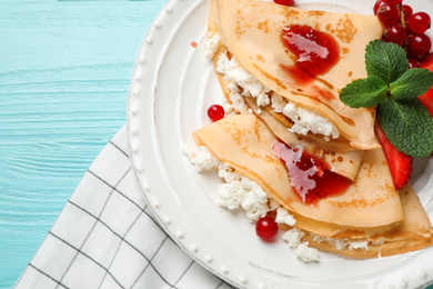 Photo of Delicious thin pancakes with cottage cheese, jam and berries on light blue wooden table, flat lay
