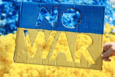 Woman holding poster in colors of Ukrainian flag with words No War and beautiful blue and yellow flowers on background, closeup