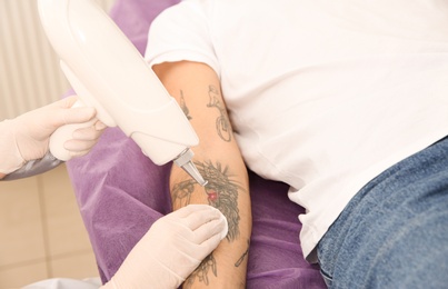 Young man undergoing laser tattoo removal procedure in salon, closeup