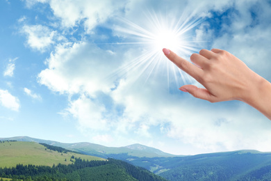 Woman holding finger near bright light, closeup. Solar energy concept