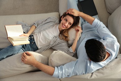 Happy couple with tablet and book on sofa in living room, above view