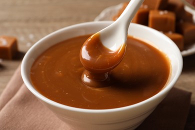 Photo of Taking yummy salted caramel with spoon from bowl at table, closeup