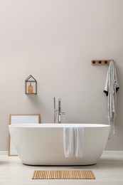 Modern ceramic bathtub near light wall indoors