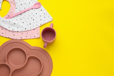 Flat lay composition with baby feeding accessories and bibs on yellow background, space for text