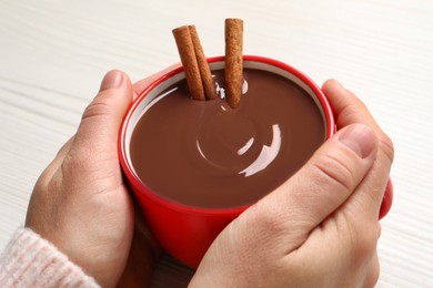 Woman holding cup of yummy hot chocolate with cinnamon on light background, closeup