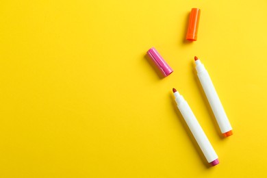 Colorful markers on yellow background, flat lay with space for text. School stationery