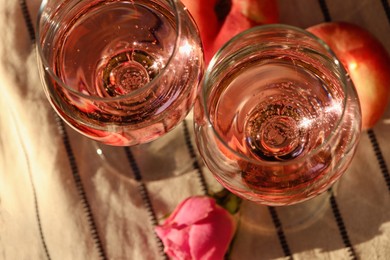 Photo of Glasses of delicious rose wine, flower and peaches on white picnic blanket outside, above view