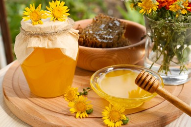Delicious honey, combs and different flowers on wooden board in garden