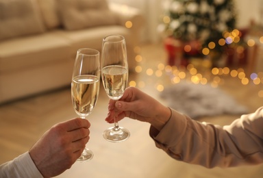 Couple clinking glasses of champagne in room decorated for Christmas, closeup. Holiday cheer and drink